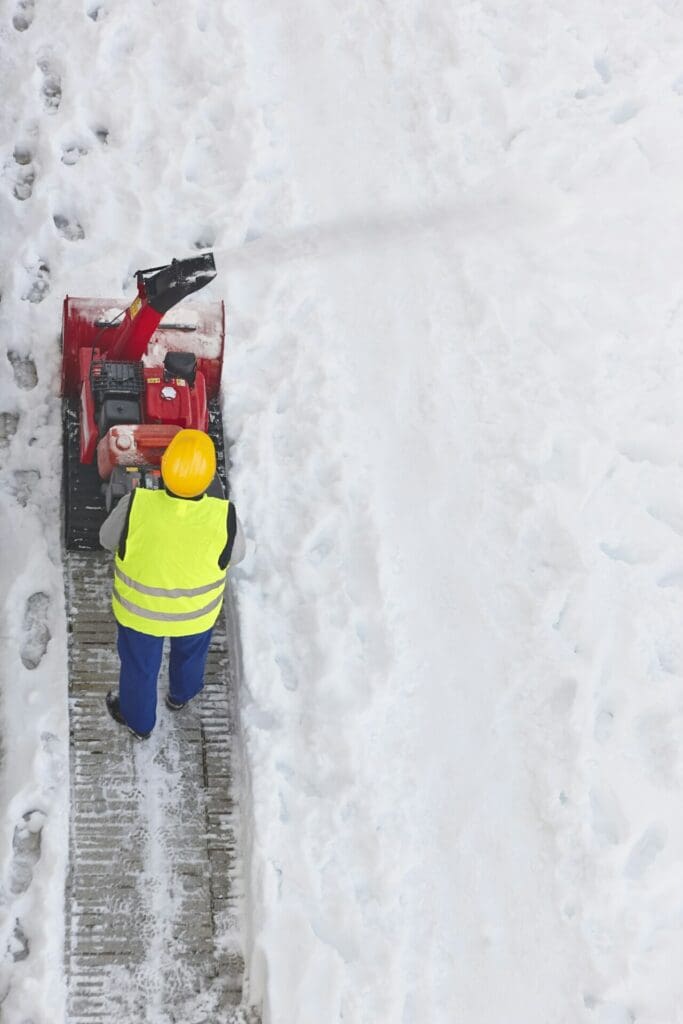 Worker cleaning snow on the sidewalk with a snowblower. Maintenance